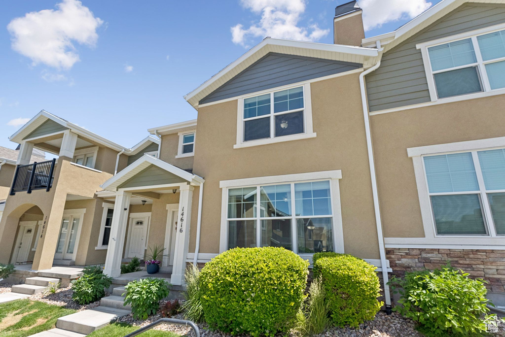 Townhome / multi-family property with a chimney, stucco siding, a balcony, and stone siding