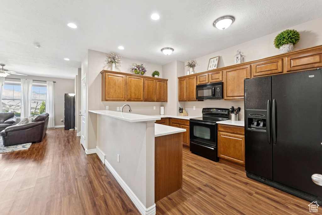 Kitchen with black appliances, brown cabinets, dark wood-type flooring, and recessed lighting
