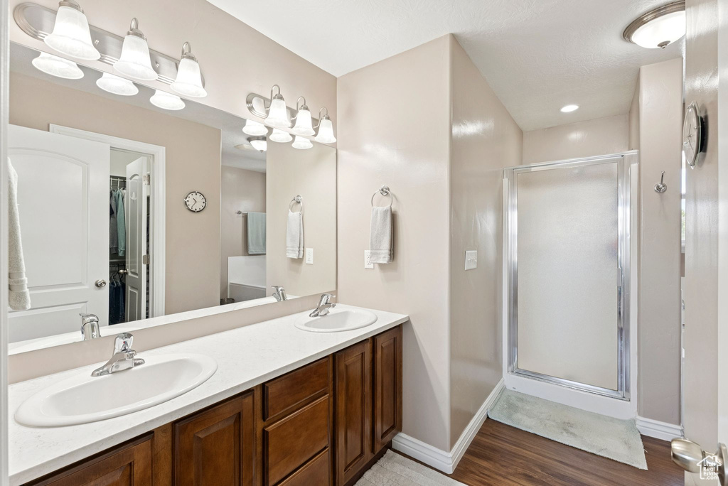 Bathroom featuring a stall shower, double vanity, and wood finished floors