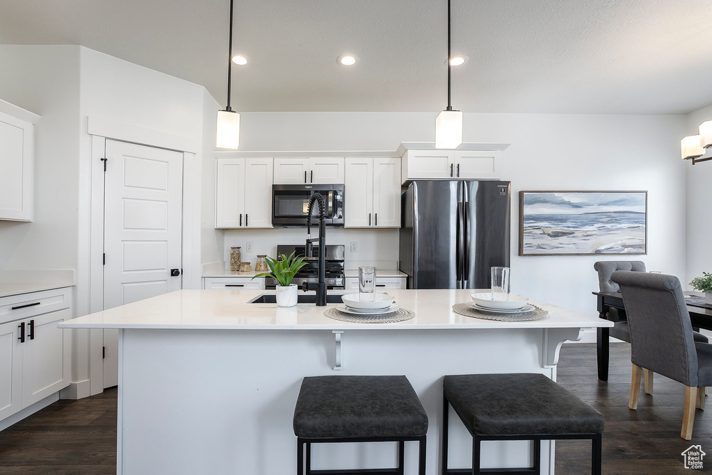 Kitchen featuring freestanding refrigerator, dark wood finished floors, a center island with sink, light countertops, and white cabinets