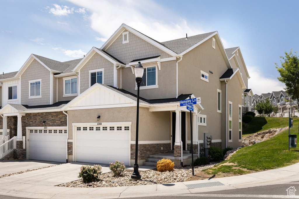 View of property with stone siding, driveway, a garage, board and batten siding, and stucco siding