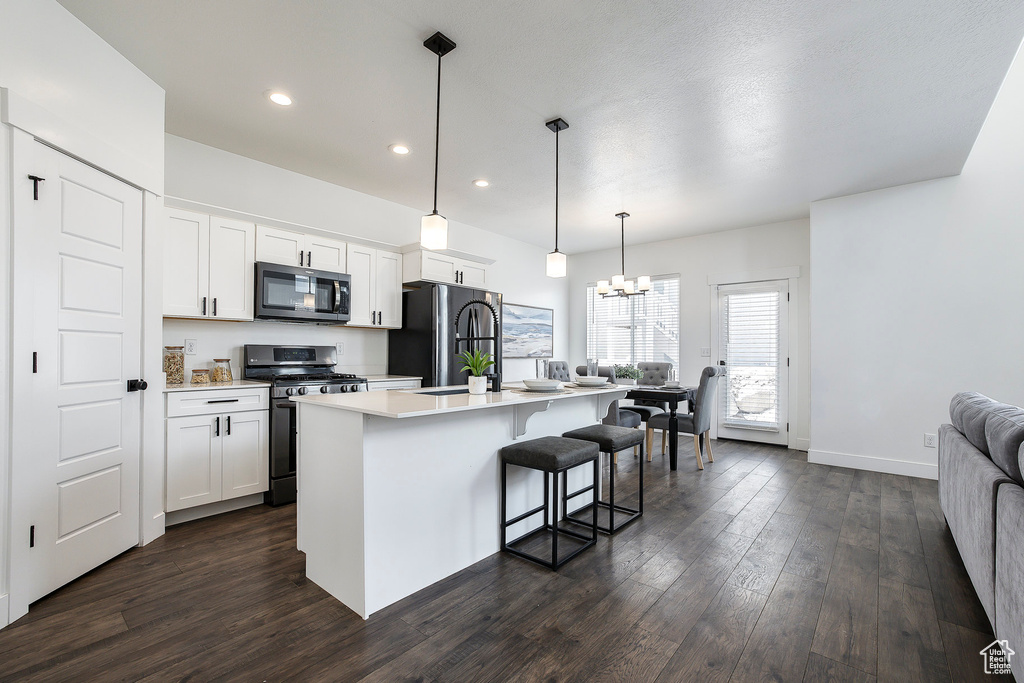 Kitchen with stainless steel range with gas cooktop, freestanding refrigerator, an island with sink, dark wood-style flooring, and a breakfast bar area