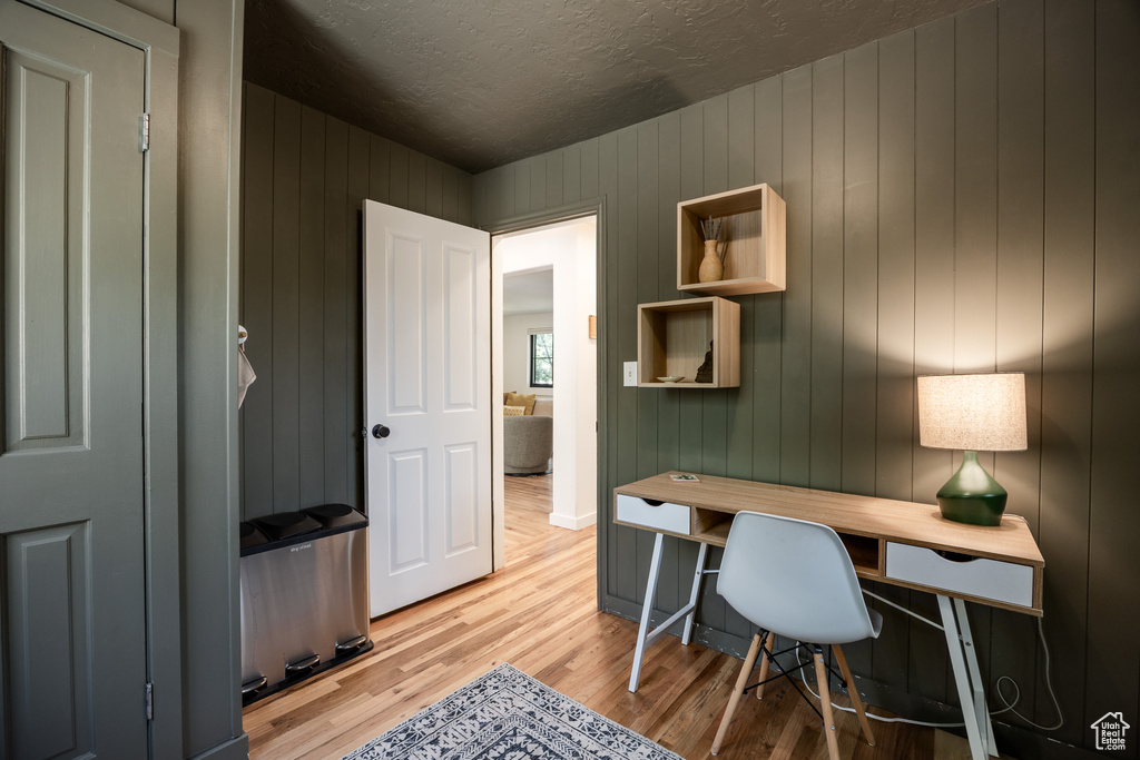 Home office with light wood-style flooring, a textured ceiling, and wooden walls