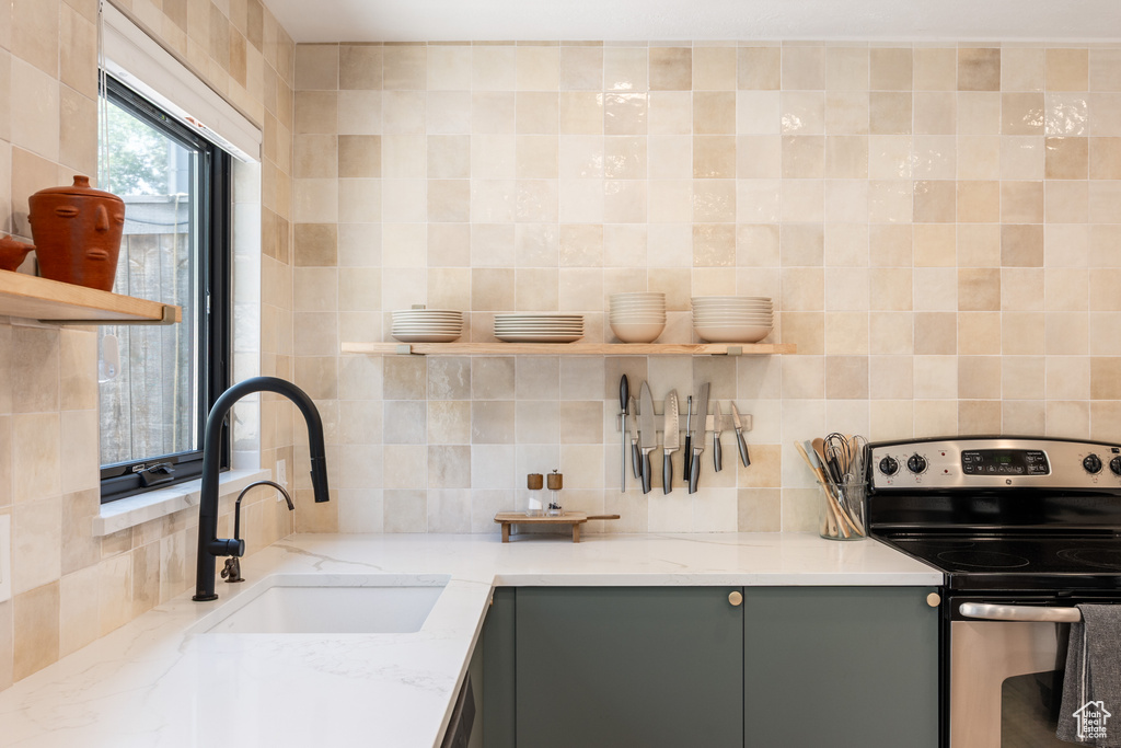 Kitchen with stainless steel electric range, open shelves, gray cabinets, backsplash, and light stone counters