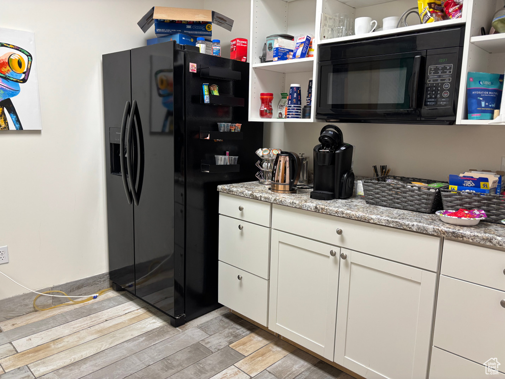 Kitchen with black appliances, open shelves, light wood-style floors, white cabinets, and light stone countertops