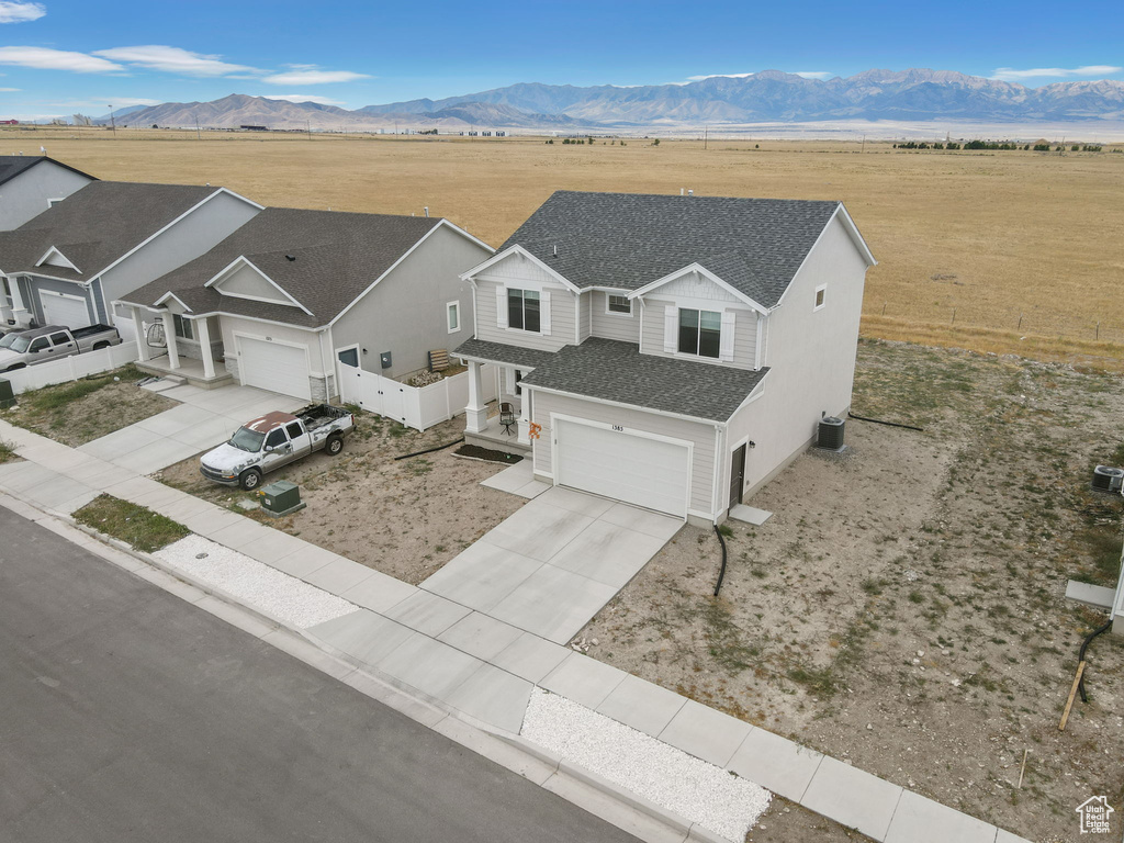 View of front of house with concrete driveway, roof with shingles, an attached garage, a mountain view, and a view of rural / pastoral area