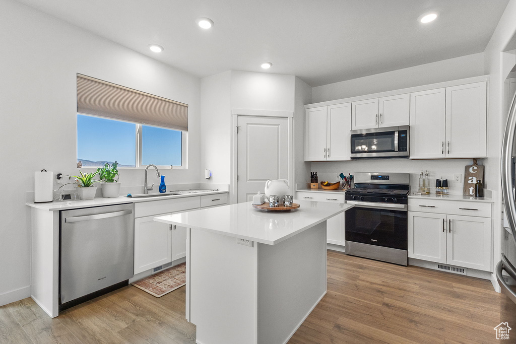 Kitchen featuring appliances with stainless steel finishes, white cabinetry, a kitchen island, light countertops, and light wood-style floors