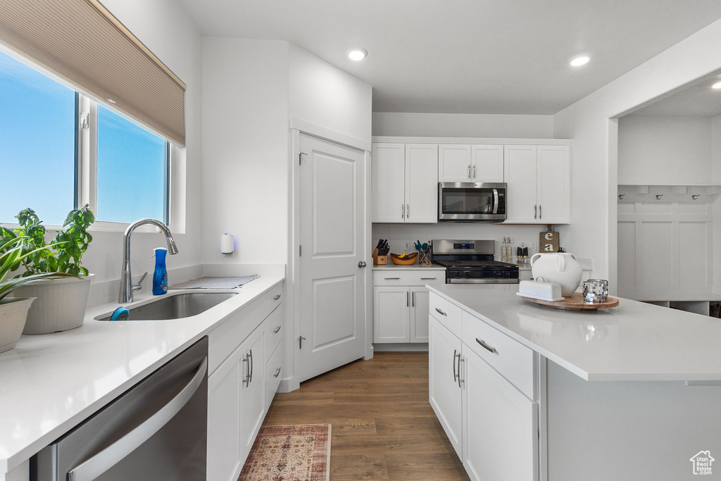 Kitchen with stainless steel appliances, recessed lighting, dark wood-type flooring, white cabinets, and a kitchen island