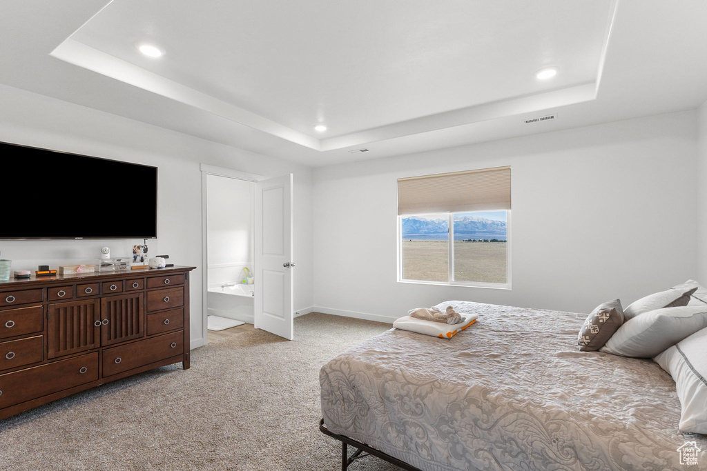 Bedroom with a tray ceiling, light carpet, recessed lighting, and ensuite bathroom