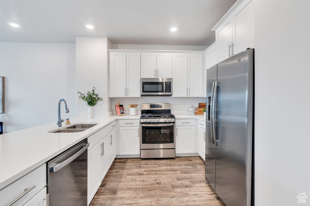 Kitchen with appliances with stainless steel finishes, light wood-type flooring, white cabinetry, light countertops, and recessed lighting