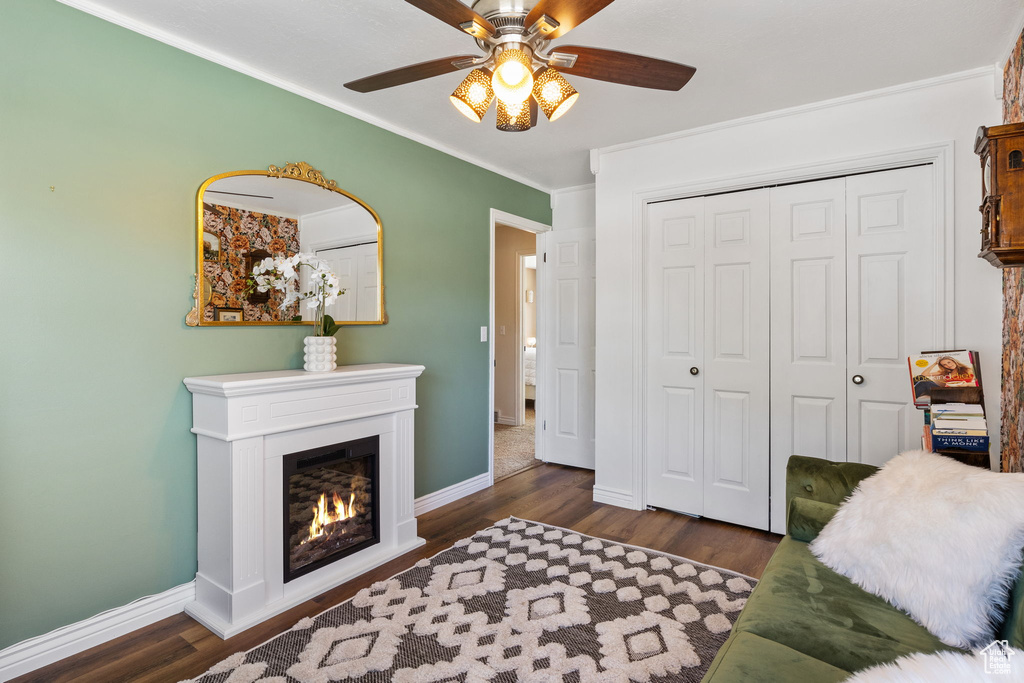 Living area with ornamental molding, ceiling fan, a lit fireplace, and dark wood-style floors