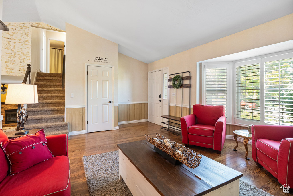 Living area featuring lofted ceiling, plenty of natural light, a wainscoted wall, stairs, and wood finished floors