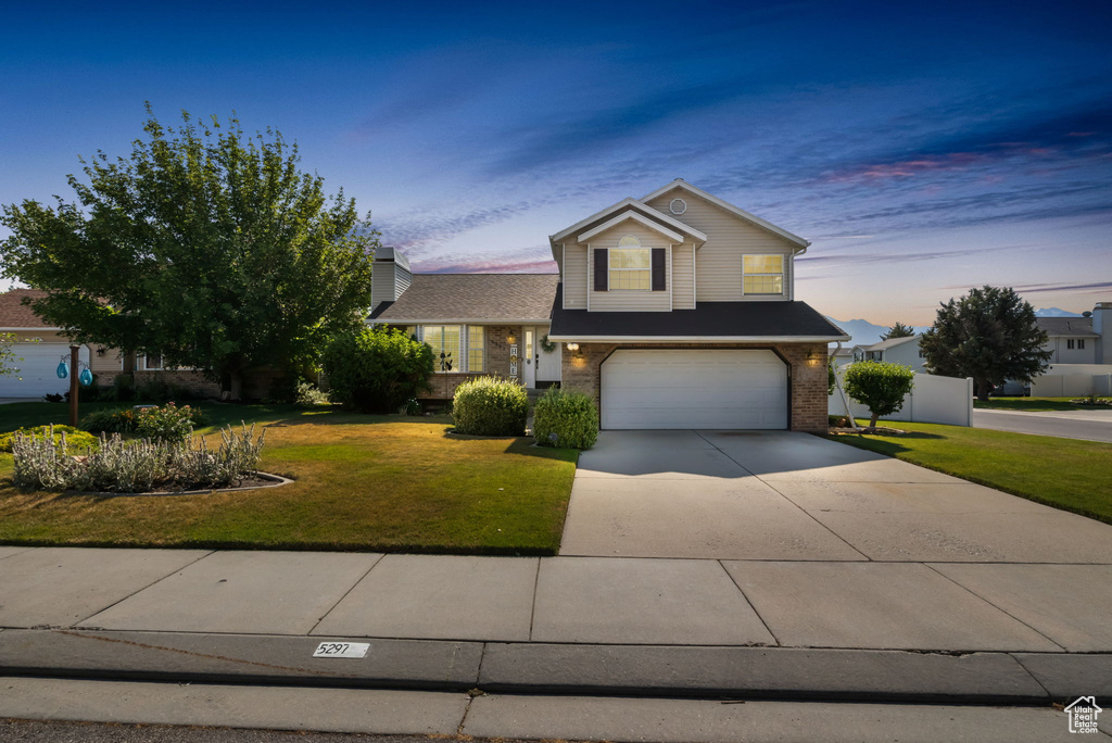 View of front facade with an attached garage, a lawn, brick siding, and driveway