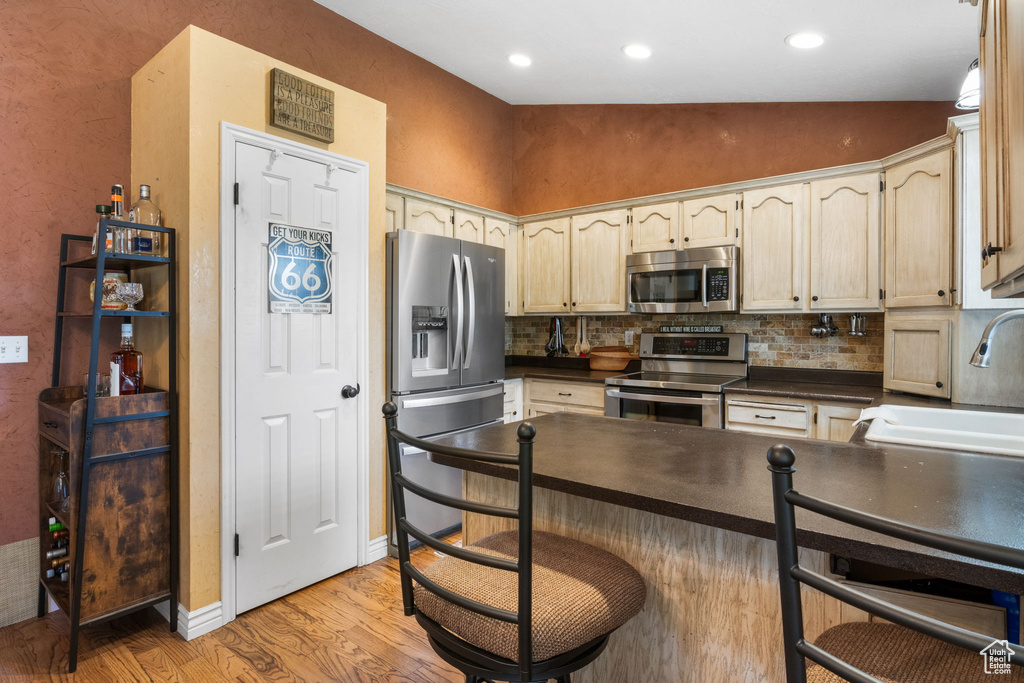Kitchen with appliances with stainless steel finishes, dark countertops, a peninsula, light wood-style floors, and decorative backsplash