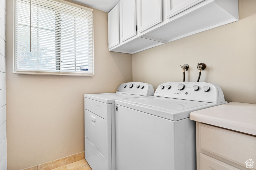 Washroom featuring cabinet space, independent washer and dryer, healthy amount of natural light, and light tile patterned floors