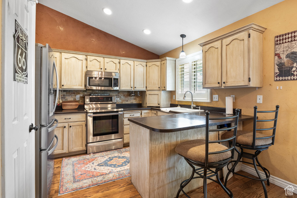 Kitchen featuring stainless steel appliances, dark countertops, a peninsula, lofted ceiling, and light wood-type flooring