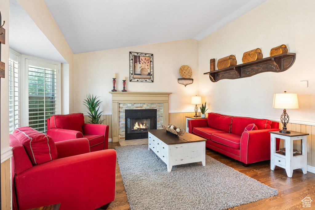 Living area featuring a wainscoted wall, wood finished floors, vaulted ceiling, and a stone fireplace