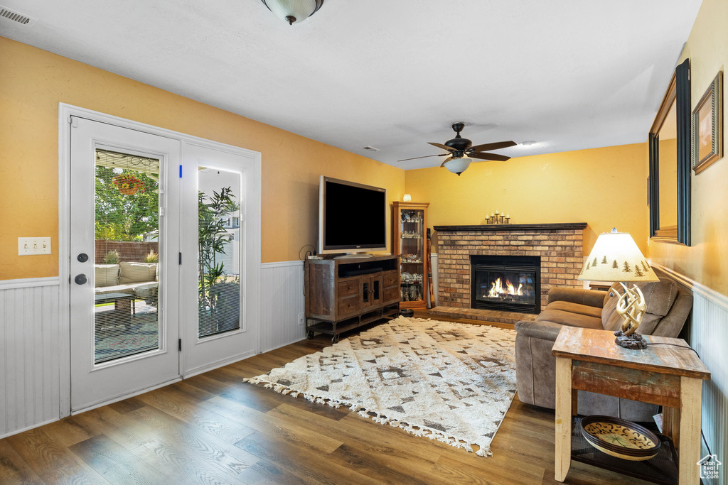 Living area featuring a wainscoted wall, wood finished floors, a brick fireplace, and ceiling fan