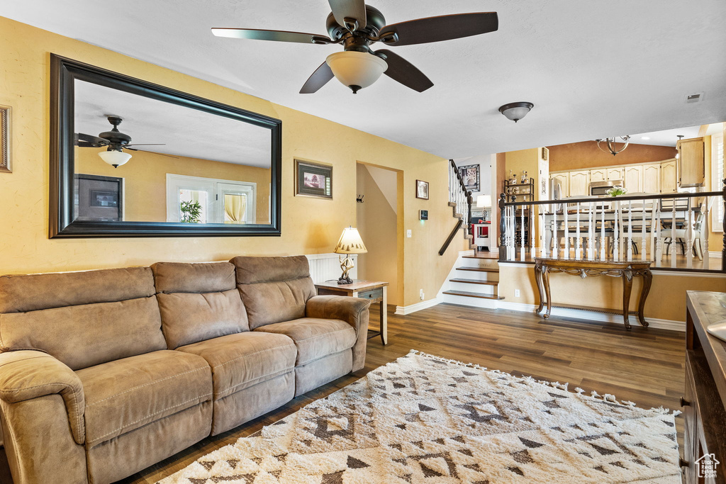 Living area with a ceiling fan, wood finished floors, and stairway