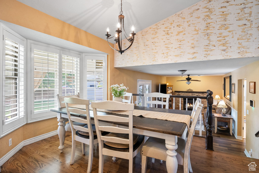 Dining area featuring a chandelier, wood finished floors, high vaulted ceiling, ceiling fan, and a fireplace