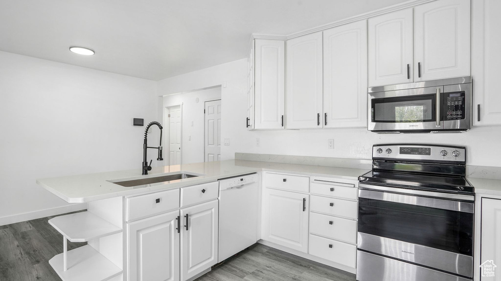 Kitchen with appliances with stainless steel finishes, a peninsula, light wood-style flooring, and white cabinetry