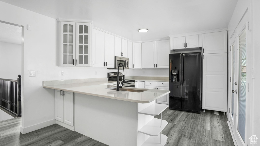 Kitchen with stainless steel appliances, wood finished floors, glass insert cabinets, white cabinetry, and a peninsula