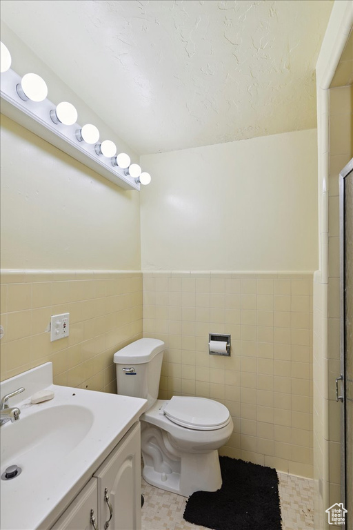 Bathroom featuring tile walls, a shower stall, vanity, and a wainscoted wall
