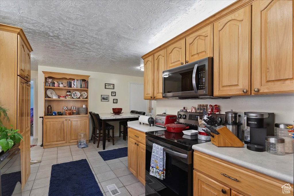 Kitchen featuring appliances with stainless steel finishes, light countertops, light tile patterned flooring, and open shelves