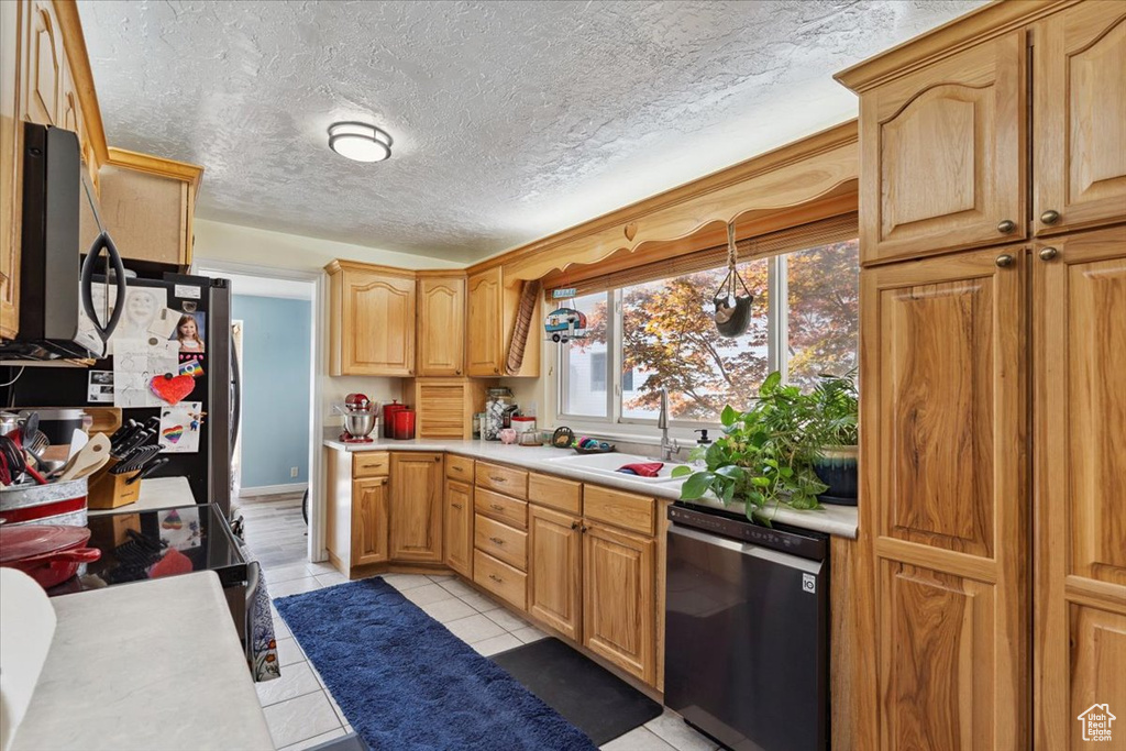 Kitchen featuring black dishwasher, light countertops, stainless steel microwave, light tile patterned floors, and a textured ceiling