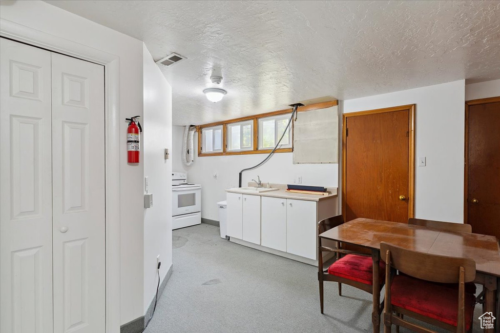 Kitchen featuring white range with electric stovetop, a textured ceiling, light countertops, light carpet, and white cabinets