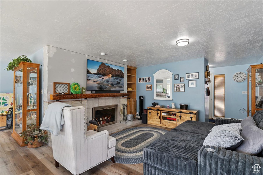 Living area with a textured ceiling, wood finished floors, a tile fireplace, and built in shelves