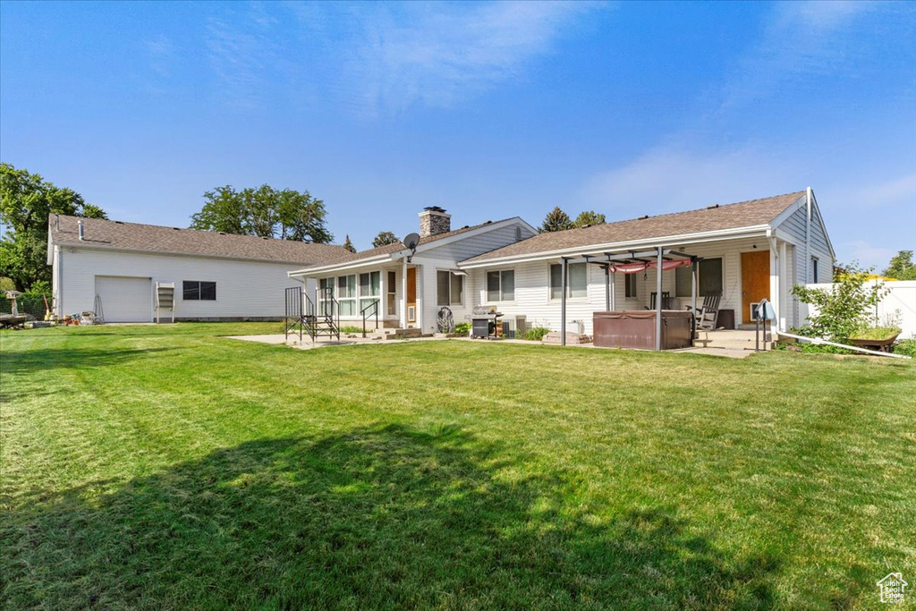 Back of property featuring a hot tub, a patio, a chimney, and a yard