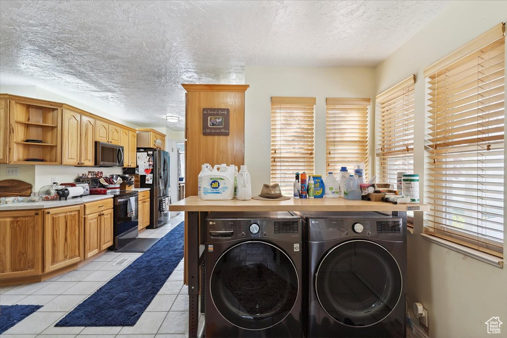 Washroom featuring a textured ceiling, washing machine and clothes dryer, and light tile patterned floors