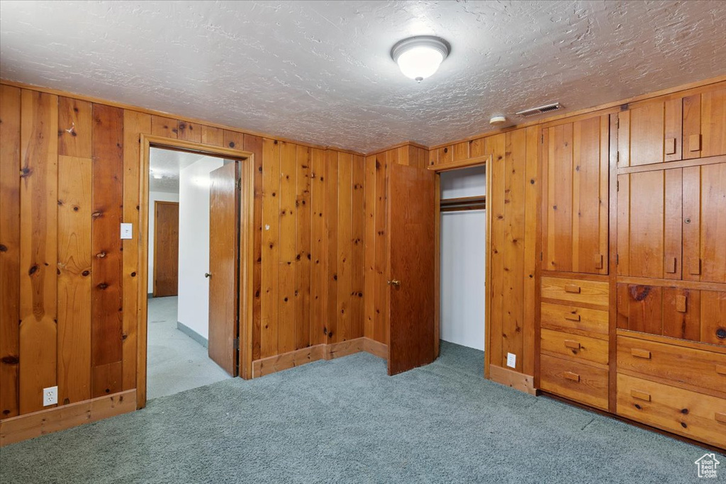 Unfurnished bedroom with carpet, wood walls, a textured ceiling, and a closet