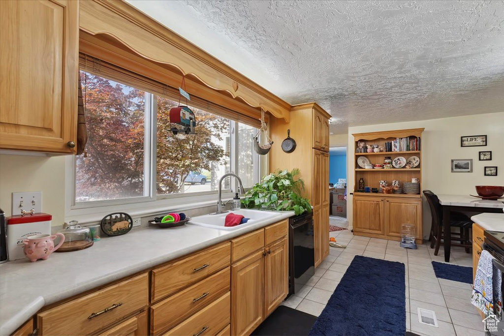 Kitchen featuring black dishwasher, light countertops, light tile patterned floors, open shelves, and a textured ceiling