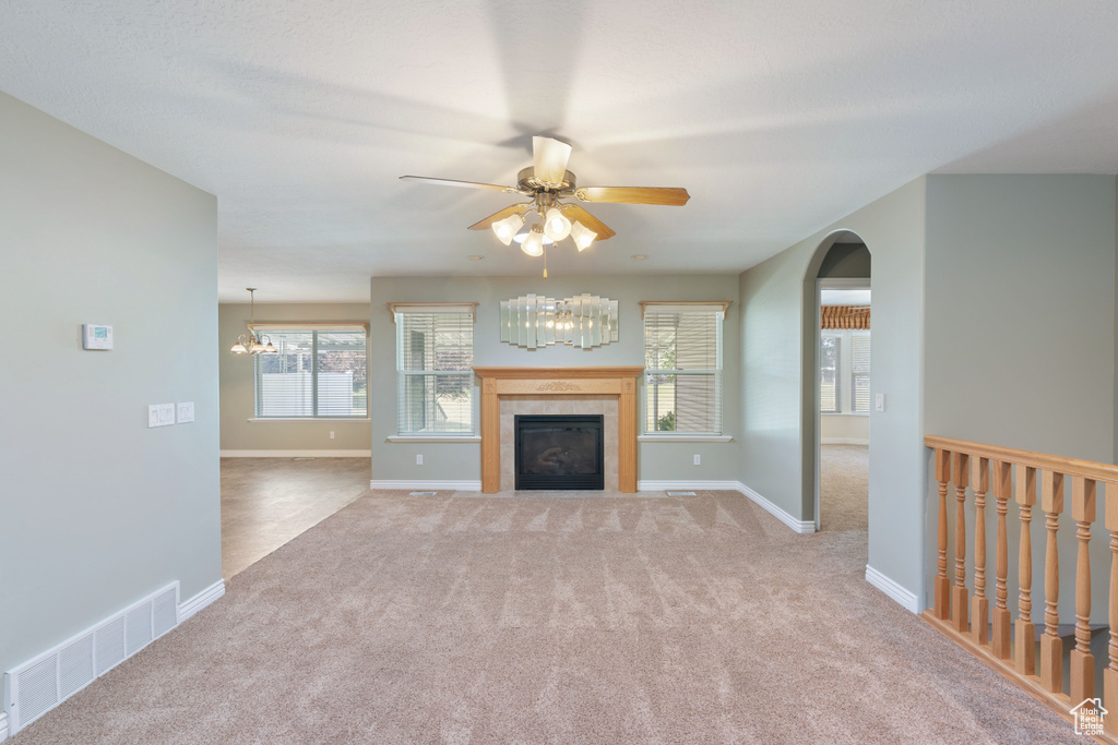 Unfurnished living room with carpet, a chandelier, ceiling fan, and a tile fireplace