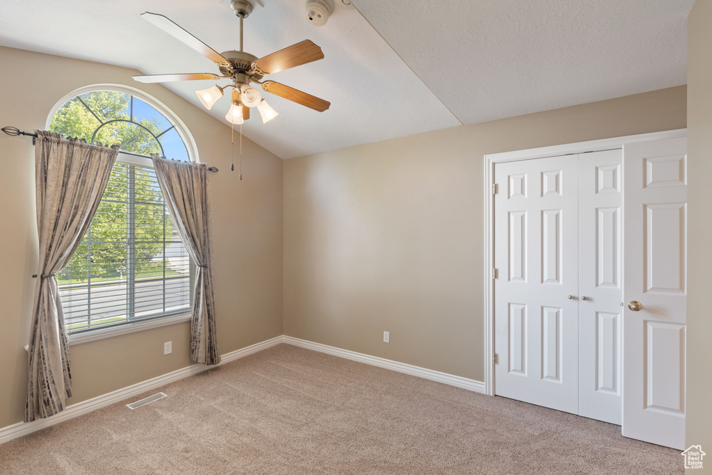 Unfurnished bedroom featuring carpet flooring, a closet, vaulted ceiling, and a ceiling fan