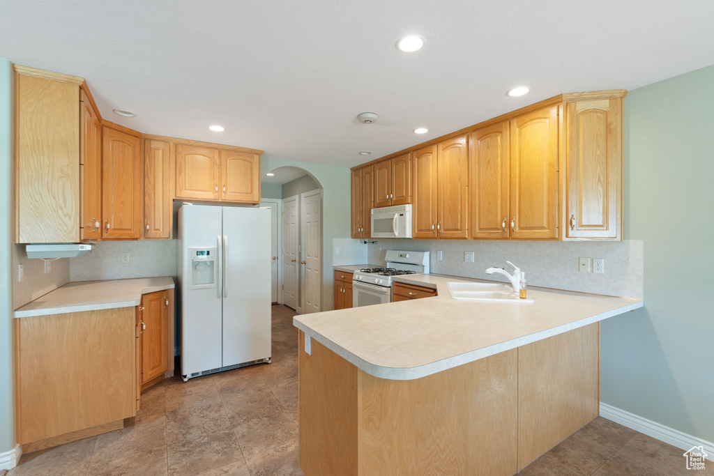 Kitchen with white appliances, arched walkways, light countertops, a peninsula, and recessed lighting
