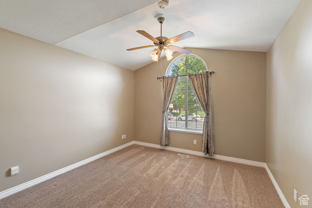 Carpeted empty room featuring ceiling fan, vaulted ceiling, and a smoke detector