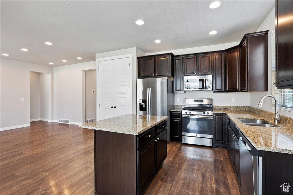 Kitchen featuring stainless steel appliances, dark wood-type flooring, a kitchen island, recessed lighting, and light stone countertops