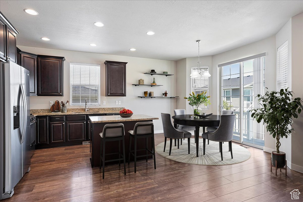 Kitchen featuring stainless steel fridge, dark brown cabinetry, dark wood-style flooring, a kitchen island, and recessed lighting