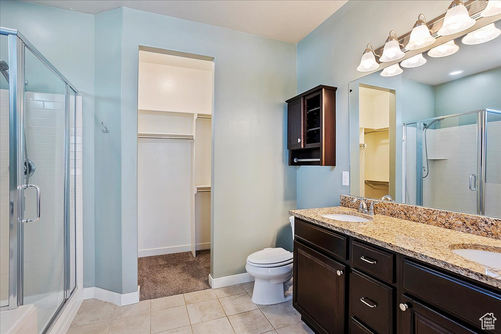 Full bath with a spacious closet, a stall shower, double vanity, and tile patterned flooring
