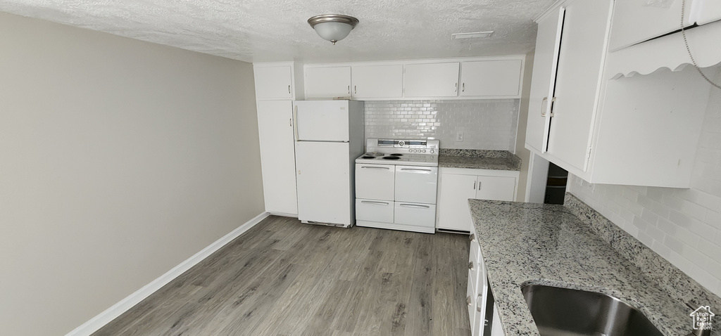 Kitchen with white appliances, decorative backsplash, wood finished floors, a textured ceiling, and white cabinetry