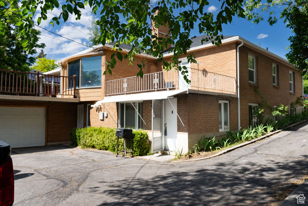 View of front of property featuring driveway, brick siding, a balcony, and an attached garage