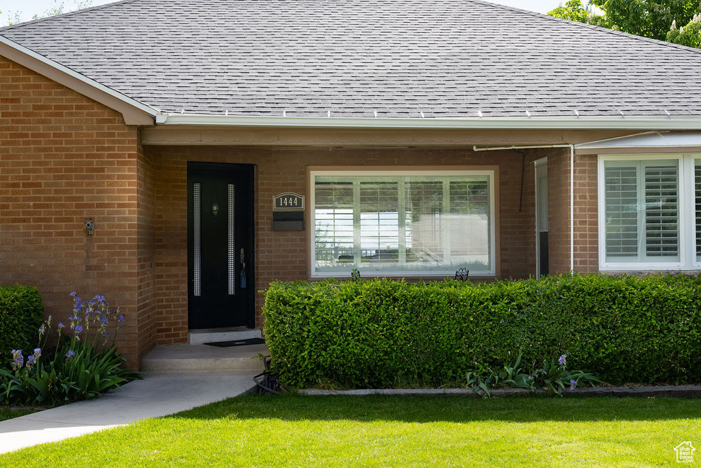 View of exterior entry featuring a shingled roof, brick siding, and a yard