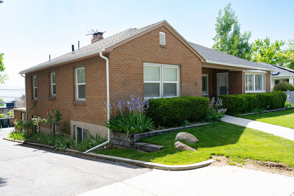 Single story home featuring brick siding, a front yard, a chimney, and a shingled roof