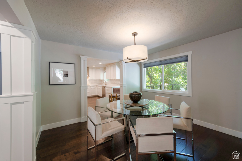 Dining room featuring dark wood finished floors, a textured ceiling, decorative columns, and recessed lighting