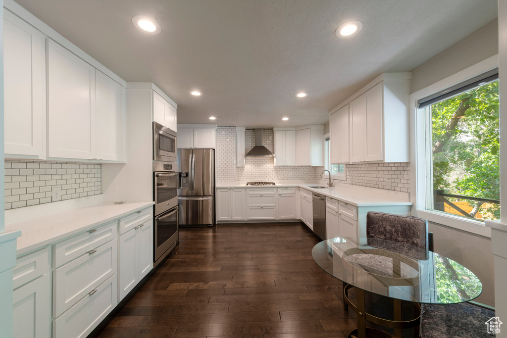 Kitchen with stainless steel appliances, wall chimney exhaust hood, dark wood finished floors, tasteful backsplash, and recessed lighting