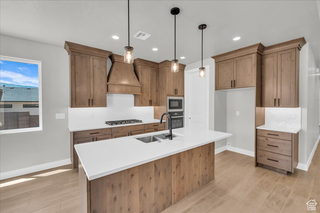 Kitchen featuring built in microwave, premium range hood, stainless steel gas stovetop, black oven, and light wood-type flooring