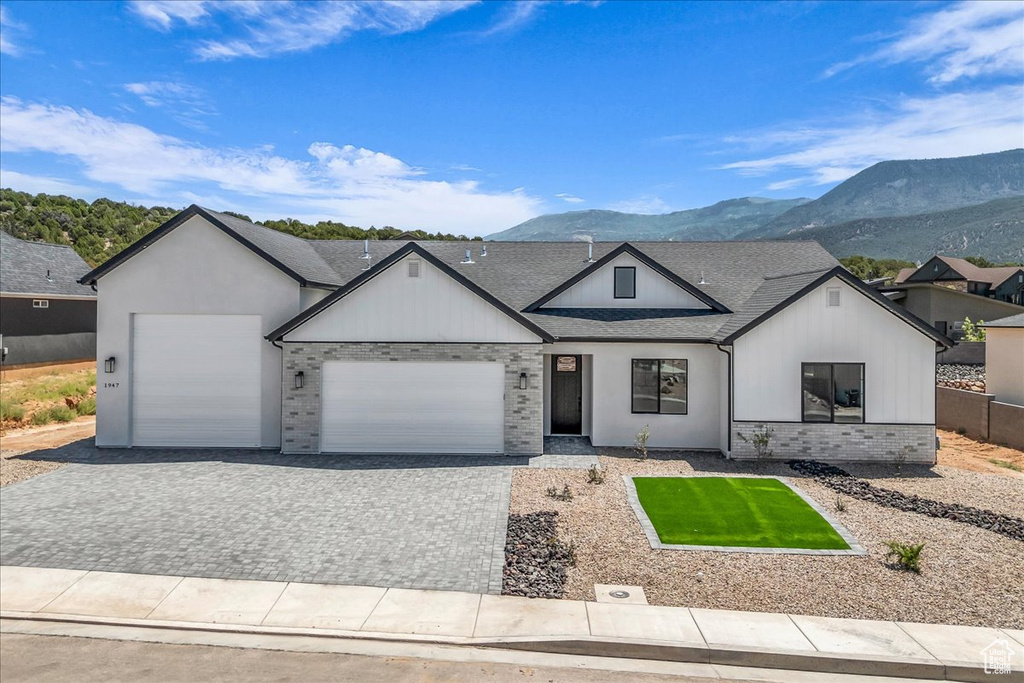 View of front of property with an attached garage, decorative driveway, a mountain view, brick siding, and roof with shingles